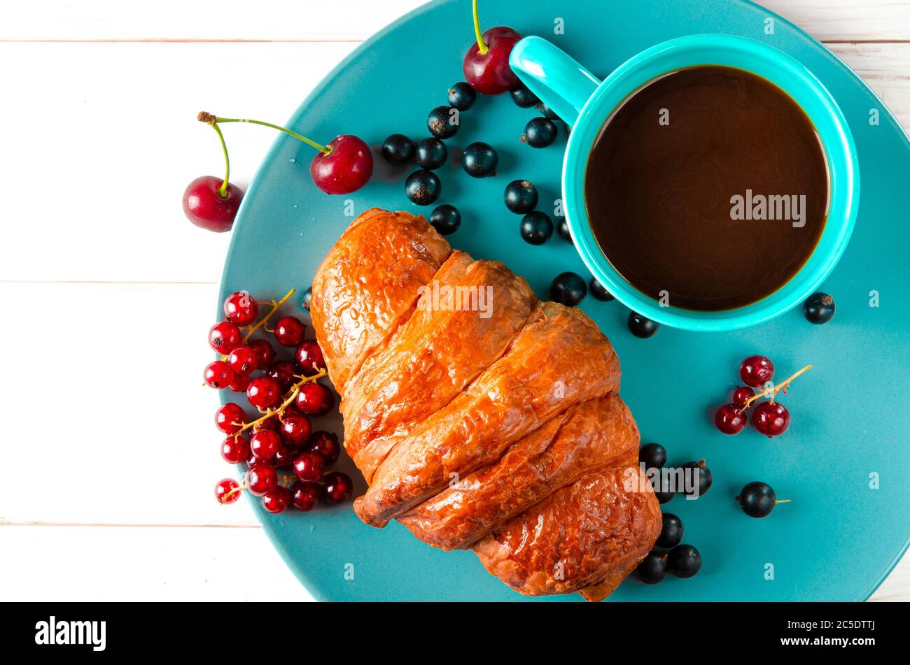 Pâtisseries maison. Un croissant rudesse aux baies se trouve sur une assiette lumineuse à côté d'une tasse de café Banque D'Images