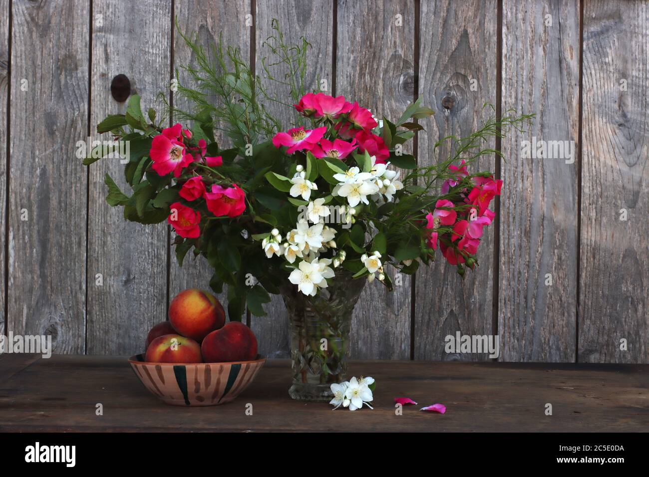 Un vase de fleurs d'été à côté d'un bol en céramique fait main rempli de pêches Banque D'Images