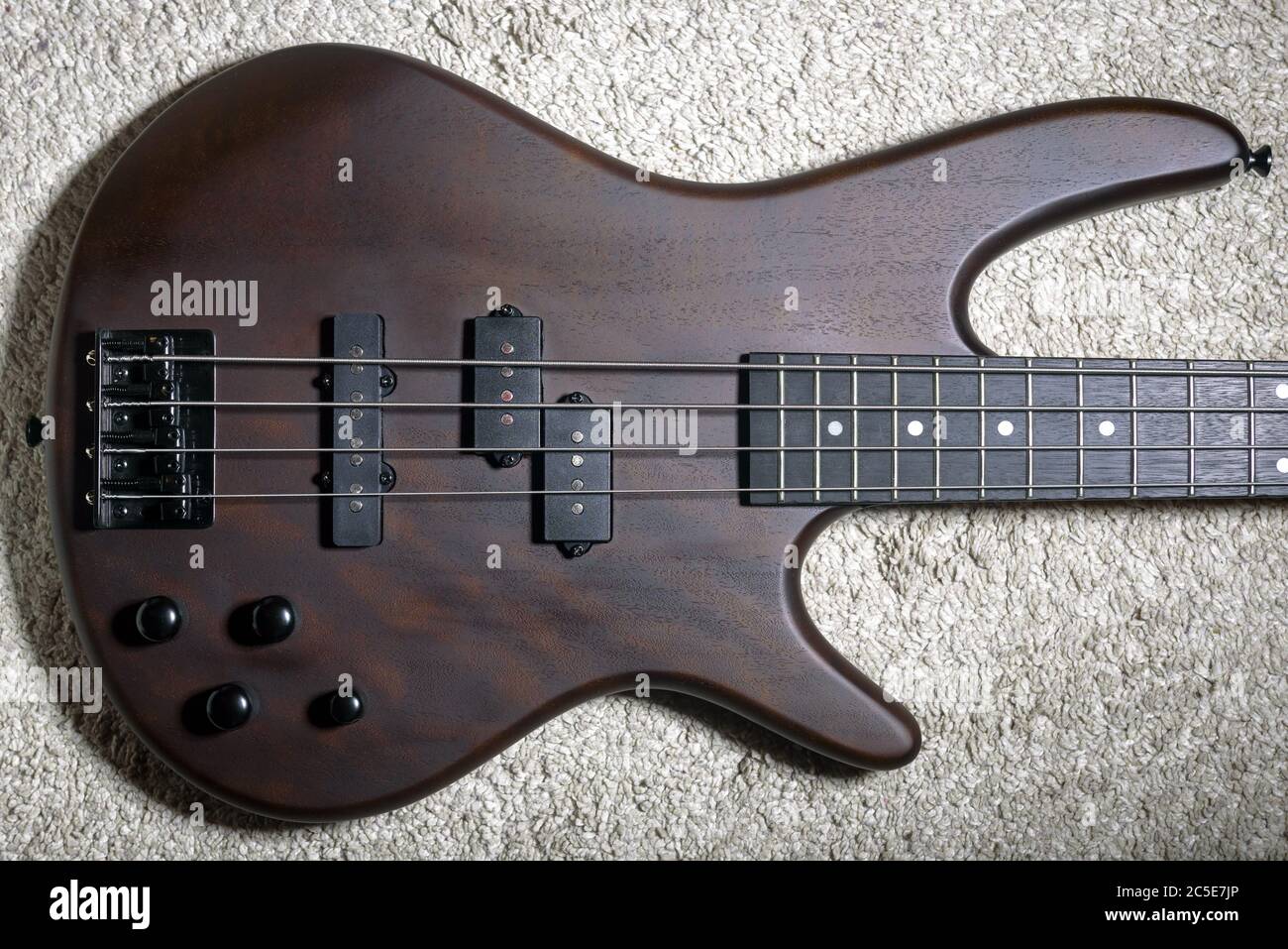 Guitare basse avec quatre cordes. Instrument de musique rock populaire. Vue de dessus du coffre électrique marron sur la moquette. Photo de guitare basse vintage avec nat Banque D'Images