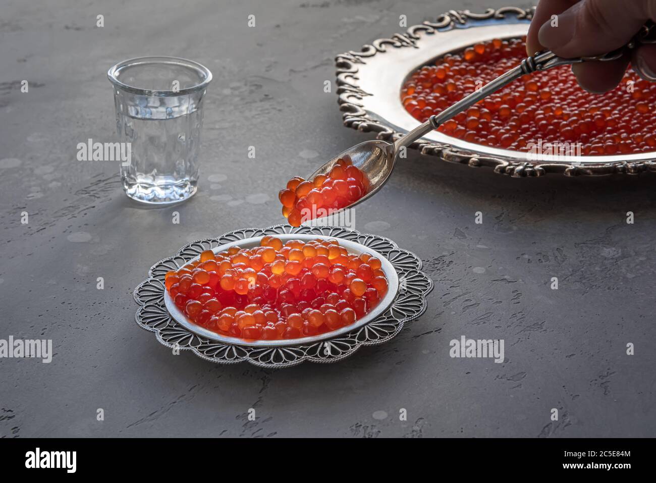 Caviar rouge en cuillère argentée et assiette sur fond gris. Vodka et un plat de caviar sur fond non focalisé. Mise au point sélective. Conce saine alimentation Banque D'Images