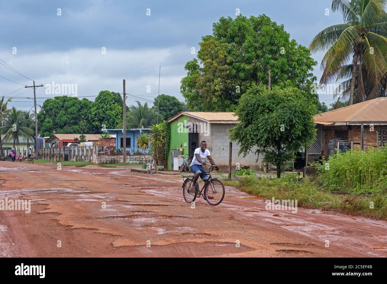 Cycliste local qui longe la route boueuse de terre dans le village de Lehem pendant la saison des pluies, région de Takutu-haute Essechibo, Guyana, Amérique du Sud Banque D'Images