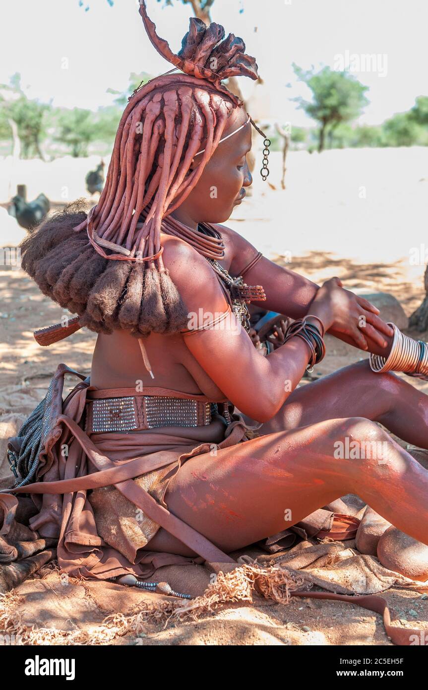 EPUPA, NAMIBIE - 27 MAI 2011 : une femme Himba mariée avec des cheveux traditionnels et une tête de lit ornée, appliquant de l'ocre rouge mélangé avec de la gelée de pétrole Banque D'Images