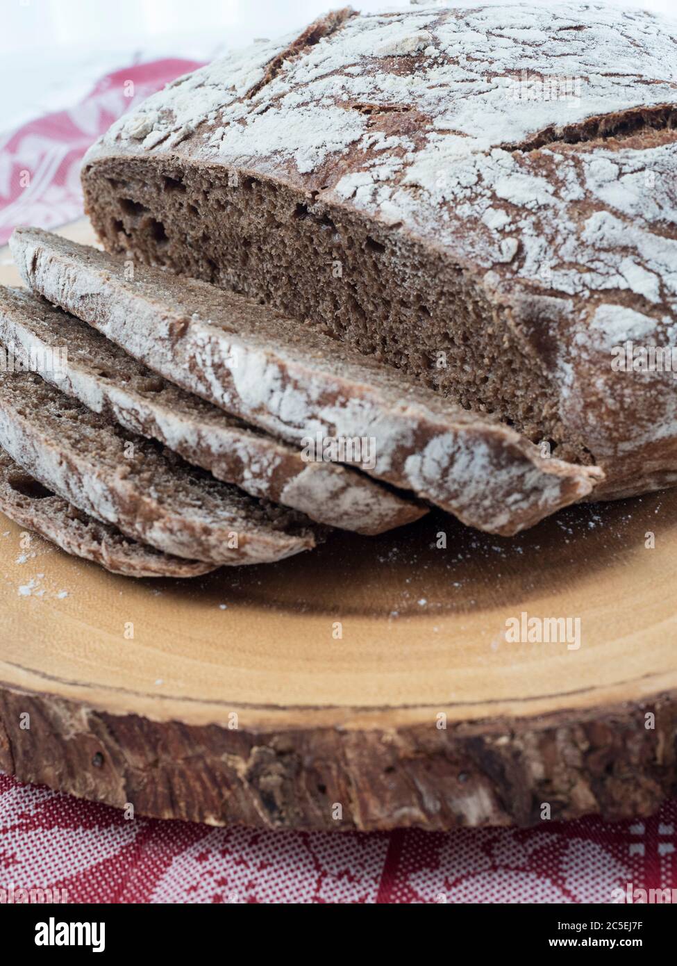 Un pain de pain de pumpernickel frais cuit au four se trouve sur une planche à pain en bois, avec des tranches coupées montrant la texture intérieure Banque D'Images