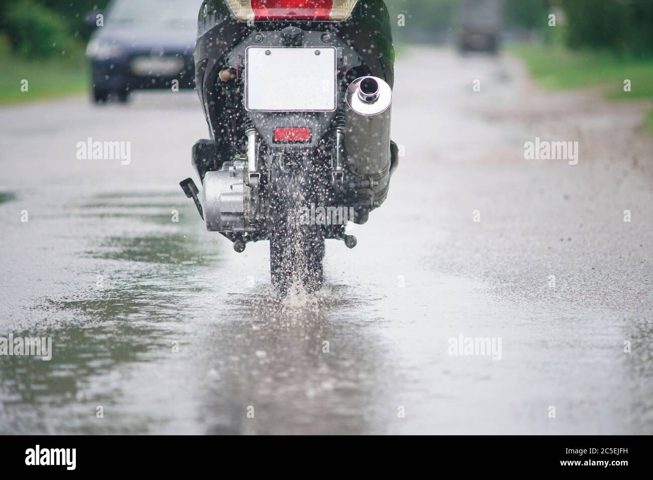 Un mobylette de moto traverse une flaque sur une route humide sous la pluie. Des projections de pulvérisation s'envolent des roues. Gros plan Banque D'Images