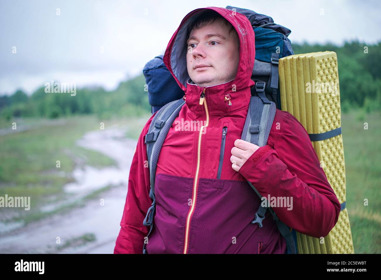Guy randonneur touristique avec sac à dos et tapis de voyage, dans une veste rouge se tient dans la pluie Banque D'Images