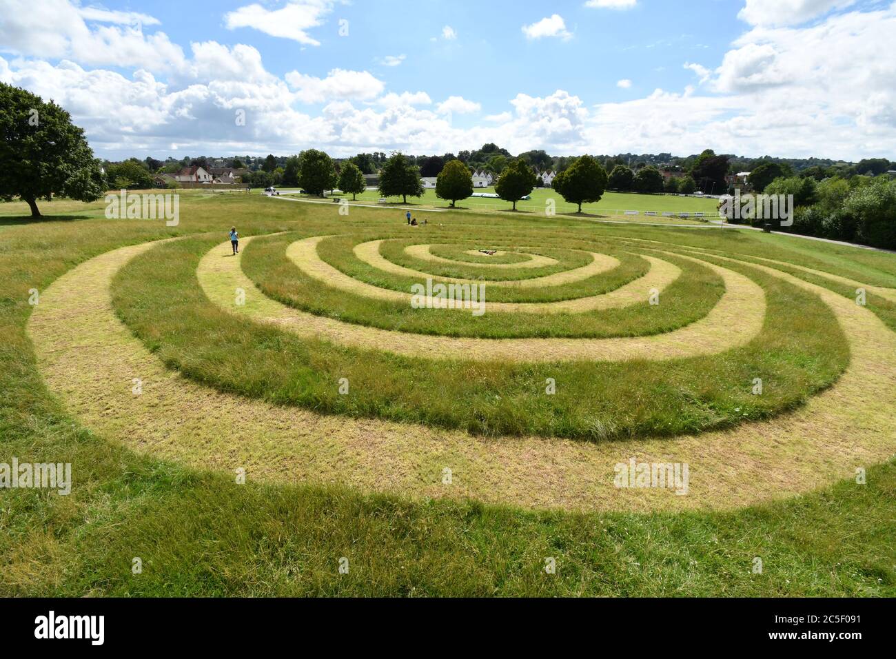 Les enfants jouent sur le chemin en spirale coupé dans l'herbe sur le vieux champ de spectacle de Frome Somerset tandis que les parents apprécient le soleil d'été.avec la ville cricke Banque D'Images