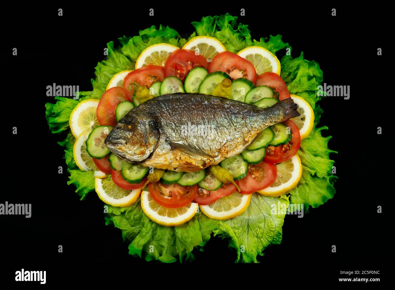 Le dorado cuit au four et le citron se trouvent sur un fond noir avec des légumes Banque D'Images