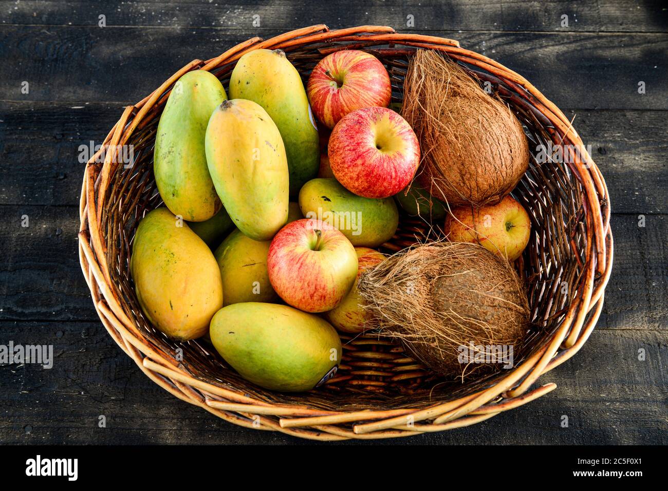 dans un panier sur fond de bois noir, mélanger les fruits, la mangue, la noix de coco et la pomme Banque D'Images