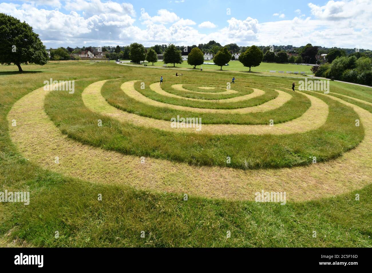 Les enfants jouent sur le chemin en spirale coupé dans l'herbe sur le vieux champ de spectacle de Frome Somerset tandis que les parents apprécient le soleil d'été.avec la ville cricke Banque D'Images