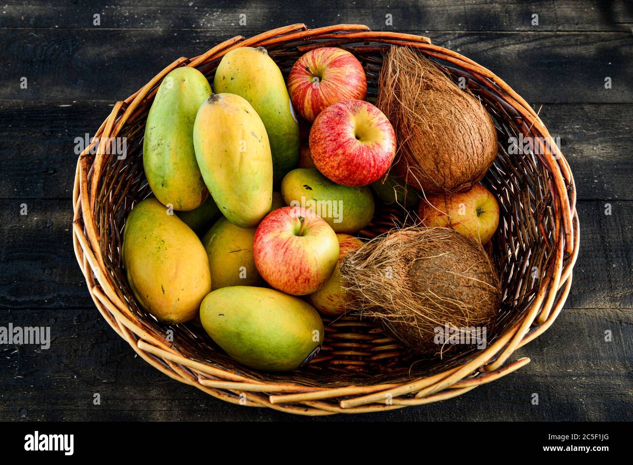dans un panier sur fond de bois noir, mélanger les fruits, la mangue, la noix de coco et la pomme Banque D'Images