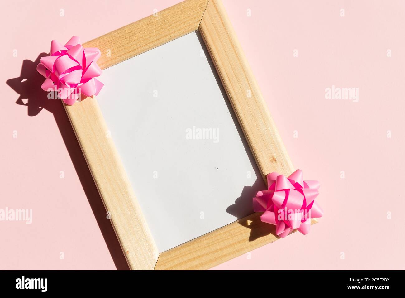 Maquette de cadre en bois avec espace pour les boîtes à affiches et à cadeaux, noeud en satin sur fond rose.boucles en ruban rose, anniversaire, mariage ou Saint-Valentin Banque D'Images