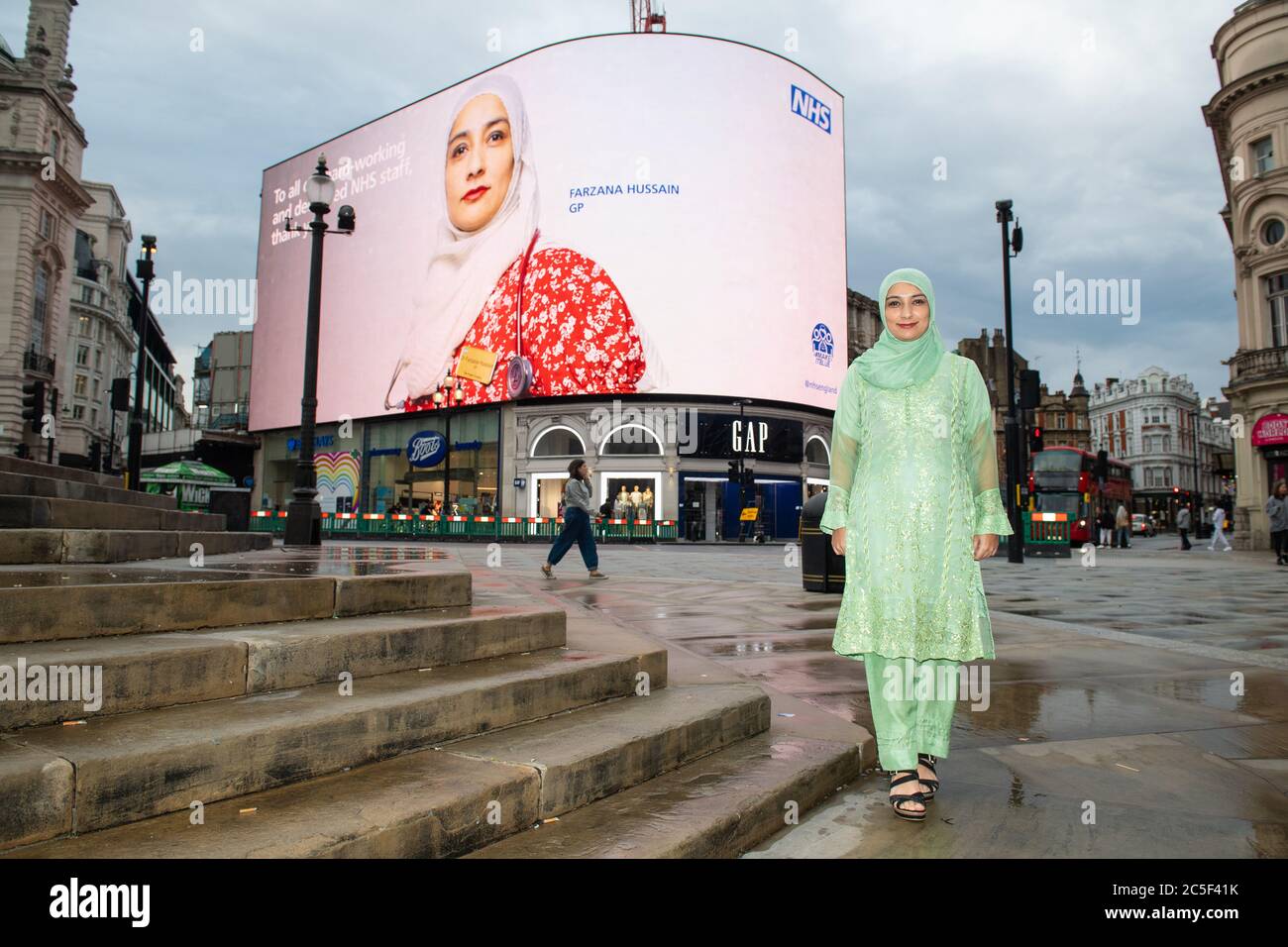 GP Farzana Hussain avec son portrait, qui fait partie d'une série prise par le photographe Rankin, comme il est exposé sur les Piccadilly Lights à Piccadilly Circus, Londres, pour marquer le 72e anniversaire du NHS. Banque D'Images