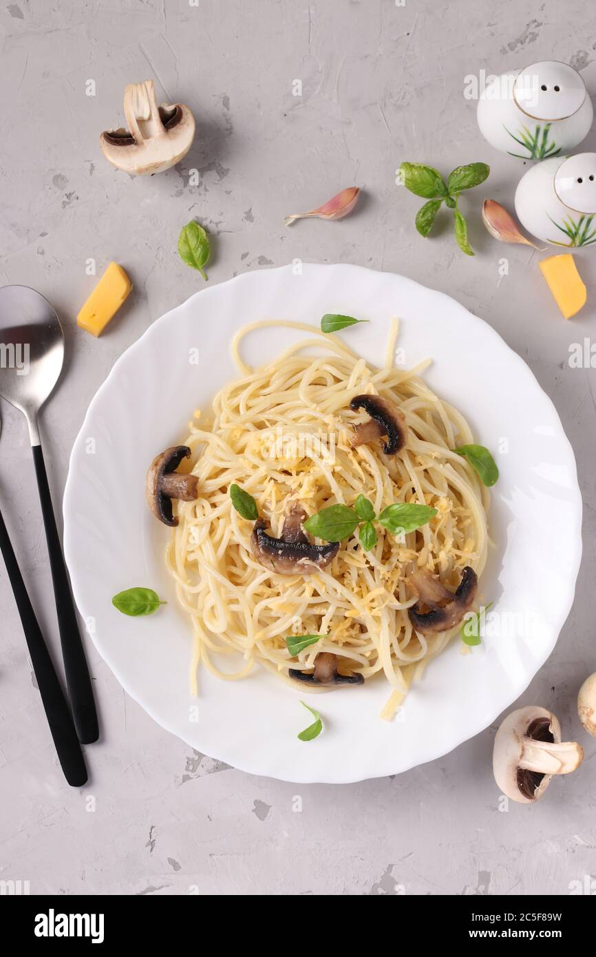 Spaghetti aux champignons et basilic sur plaque blanche sur fond gris, gros plan Banque D'Images