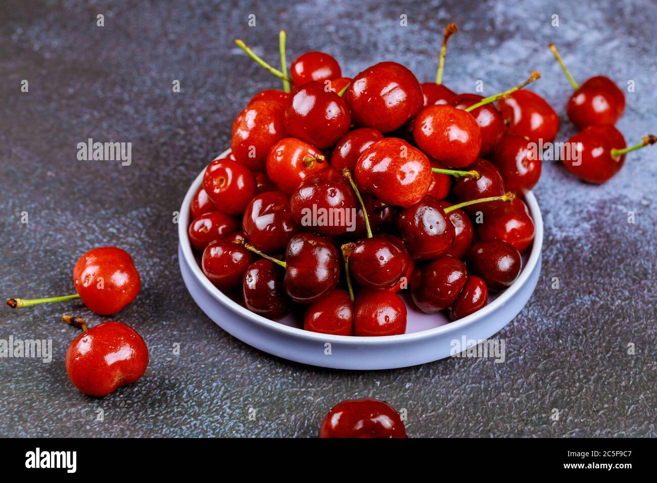 Cerises naturelles brillantes avec tige dans plaque sur fond gris. Banque D'Images
