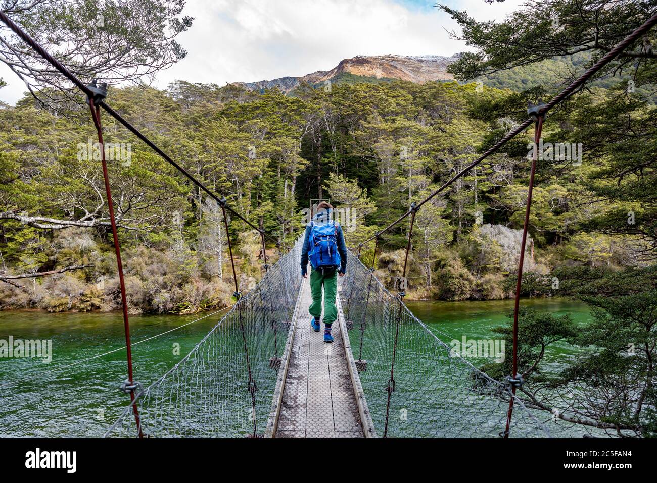 Jeune homme sur un pont suspendu au-dessus de la rivière Mavora, Mavora, Southland, South Island, Nouvelle-Zélande Banque D'Images