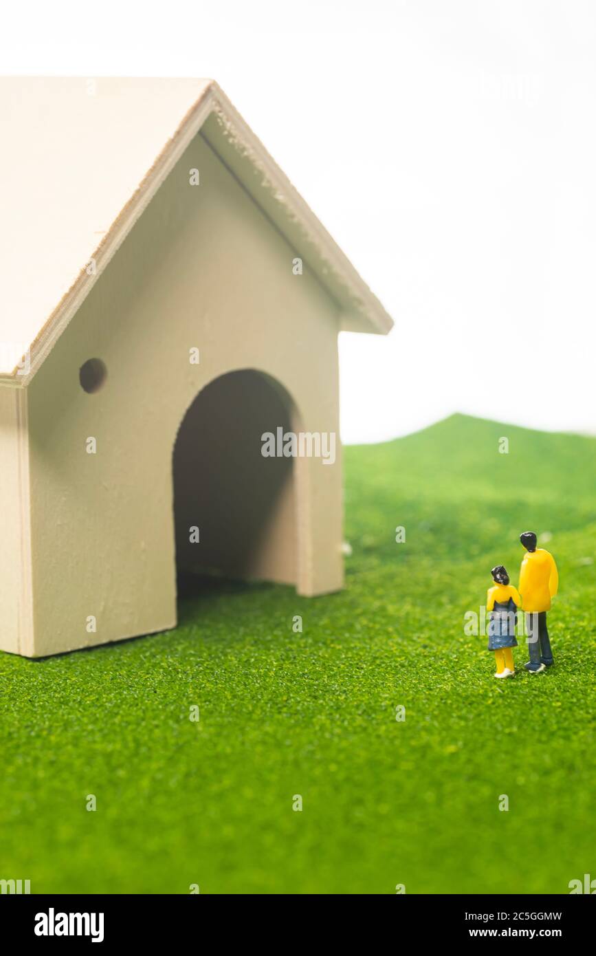 Figurines de couple miniature devant une maison de jouet, achetant ou possédant un concept de maison Banque D'Images