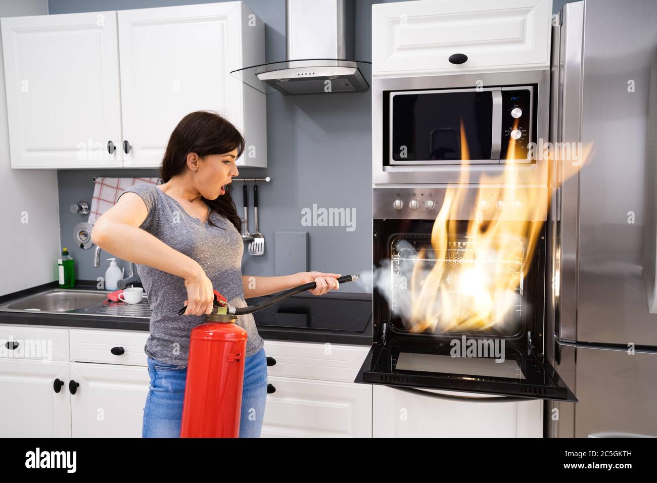 Jeune femme à l'aide d'extincteur pour éteindre le feu du four à la maison Banque D'Images