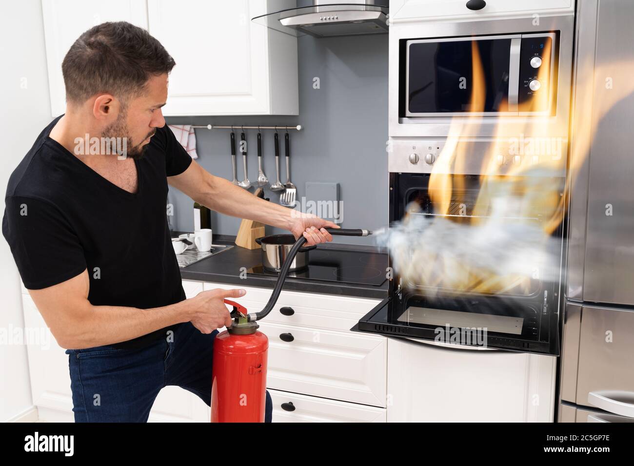 Homme utilisant un extincteur pour mettre le feu du four à la maison Banque D'Images