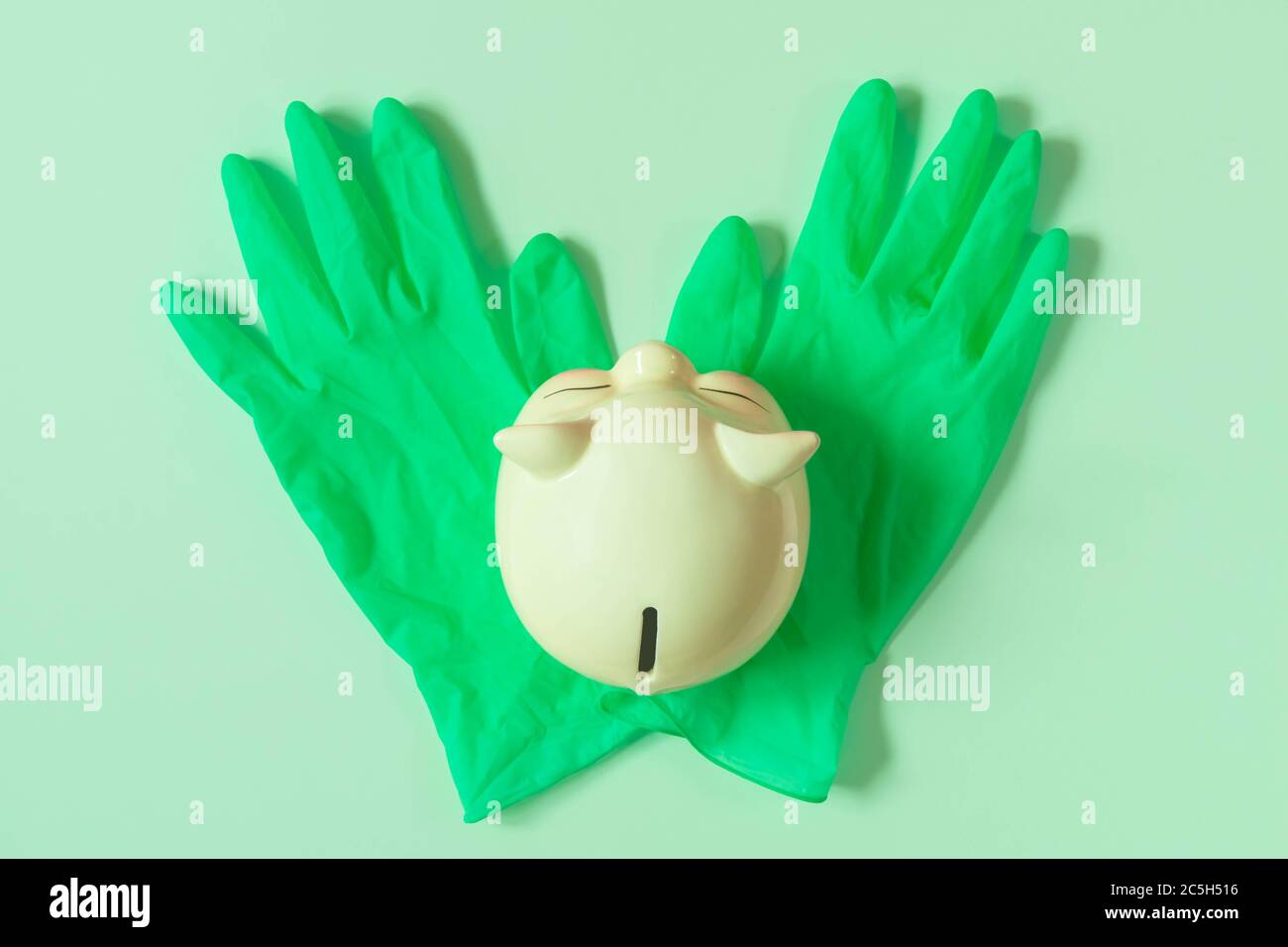 Tirelire sur des gants en latex vert isolés sur un fond vert clair. Vue de dessus de la cale de porc sur des gants en caoutchouc. Concept de financement et d'épargne Banque D'Images