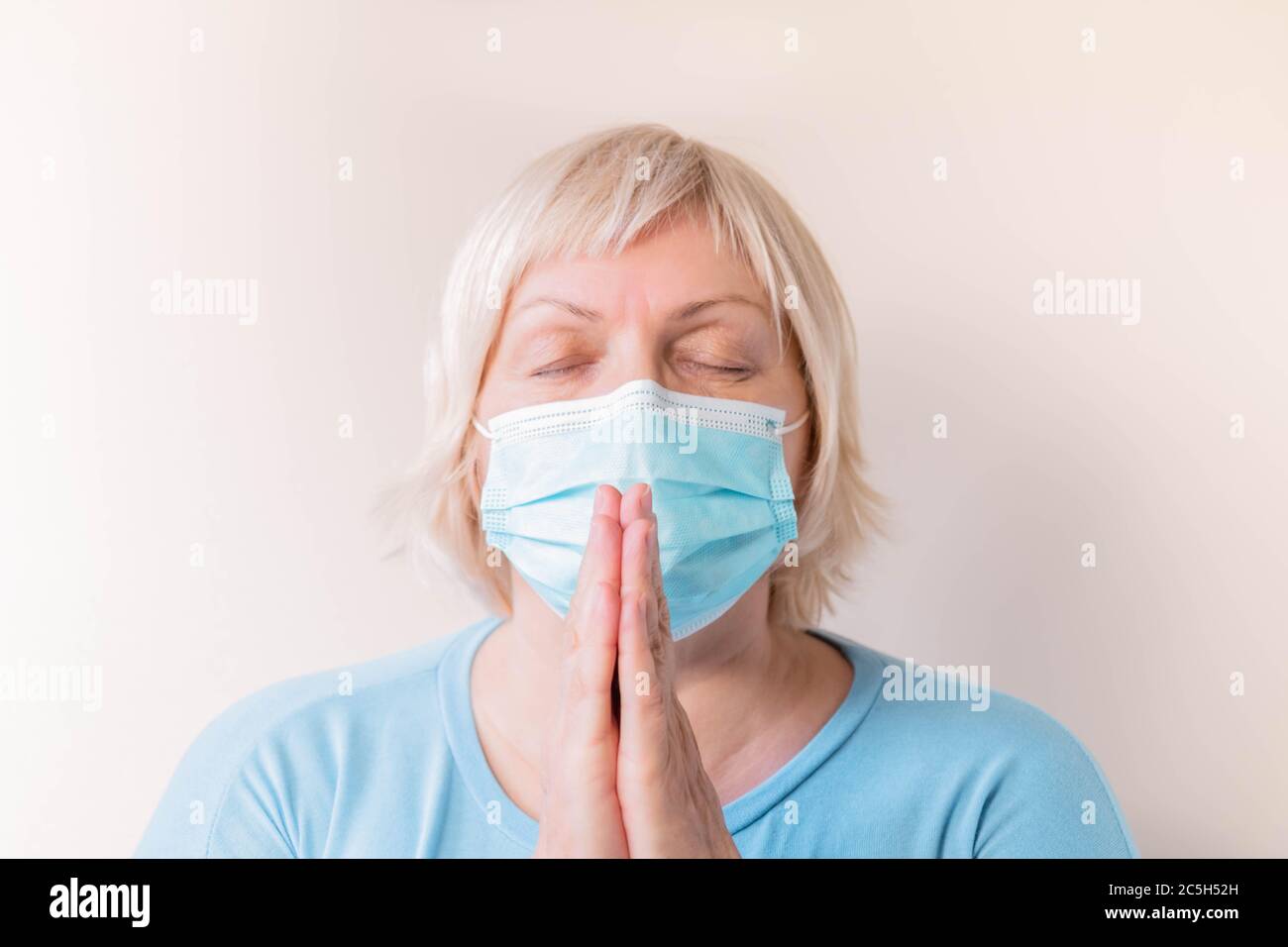Femme âgée avec masque facial priant. Portrait d'une femme âgée dans un masque médical priant. Femme mature tenant les mains dans la prière. Priez à la maison Banque D'Images