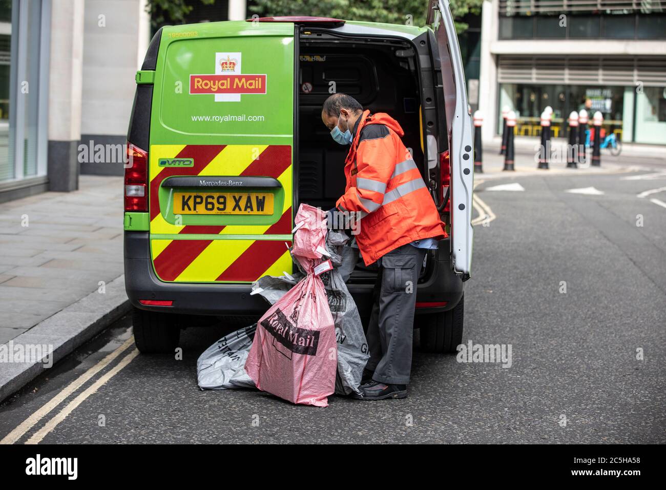 Employé de livraison postale se préparant à charger son Royal Mail Zero Emission Electric postal Van portant un masque facial dans le centre de Londres, Angleterre, Royaume-Uni Banque D'Images