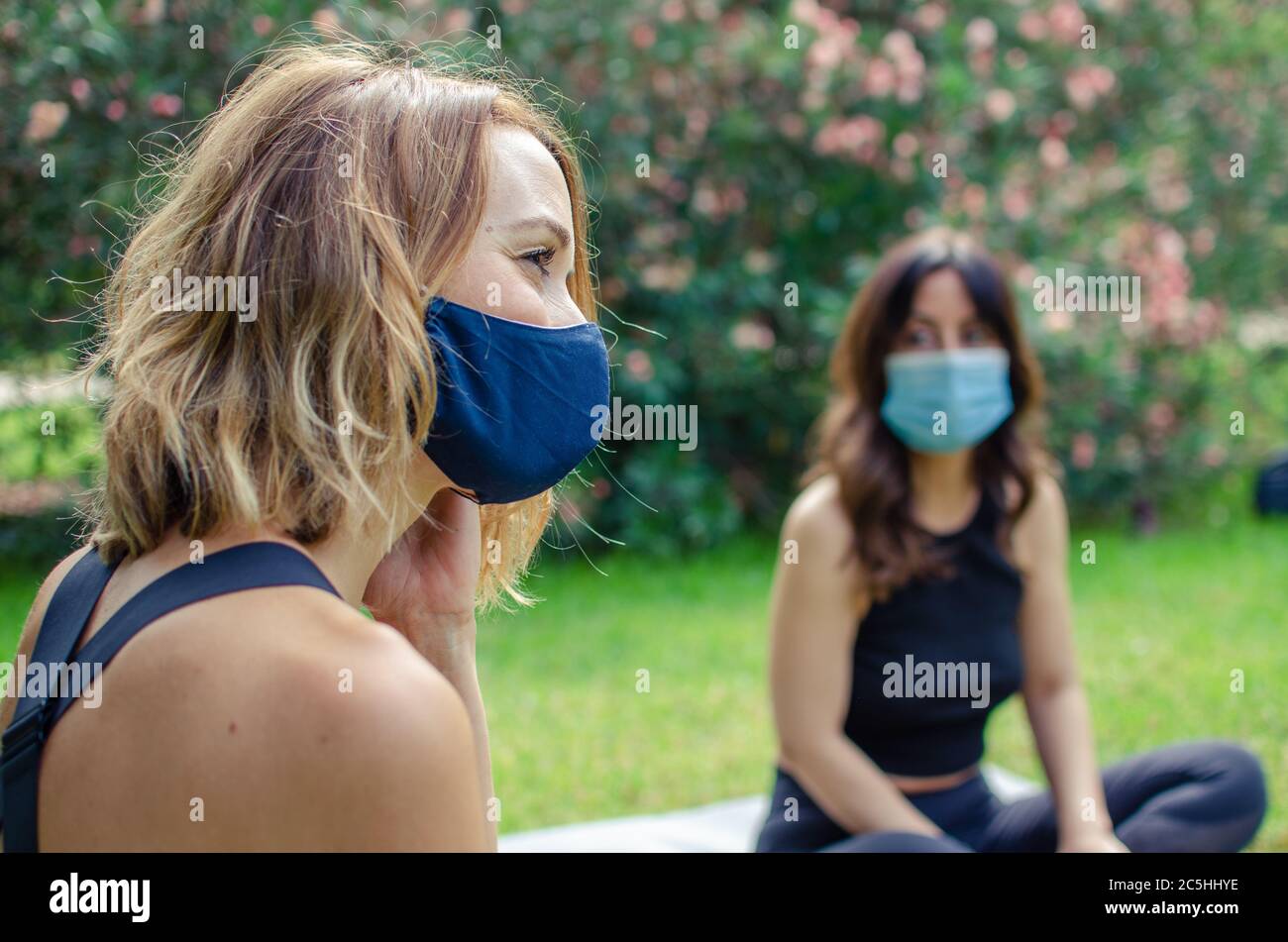Deux femmes parlent dans un parc avec des masques. Ils sont assis sur l'herbe Banque D'Images