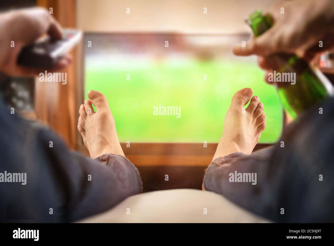 Homme assis sur un canapé, regardant un match à la télévision avec télécommande et bière à la maison Banque D'Images