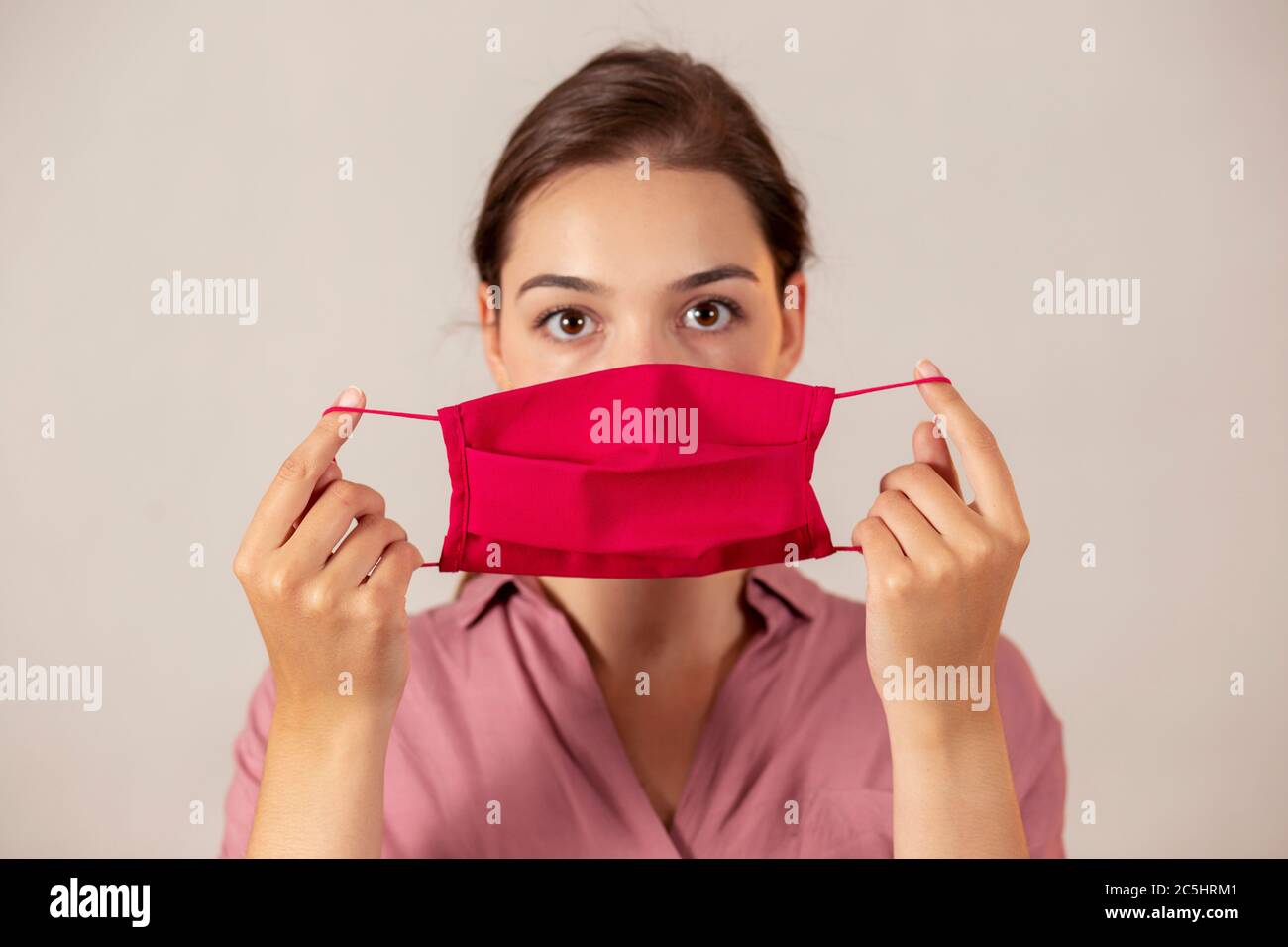 Jeune infirmière tenant un masque rouge devant elle, se préparant à le mettre. Banque D'Images