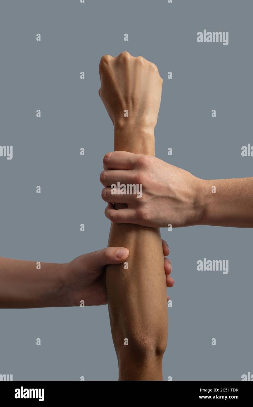 Gros plan de deux mains à peau claire tenant le poignet et l'avant-bras d'une main à peau foncée Banque D'Images