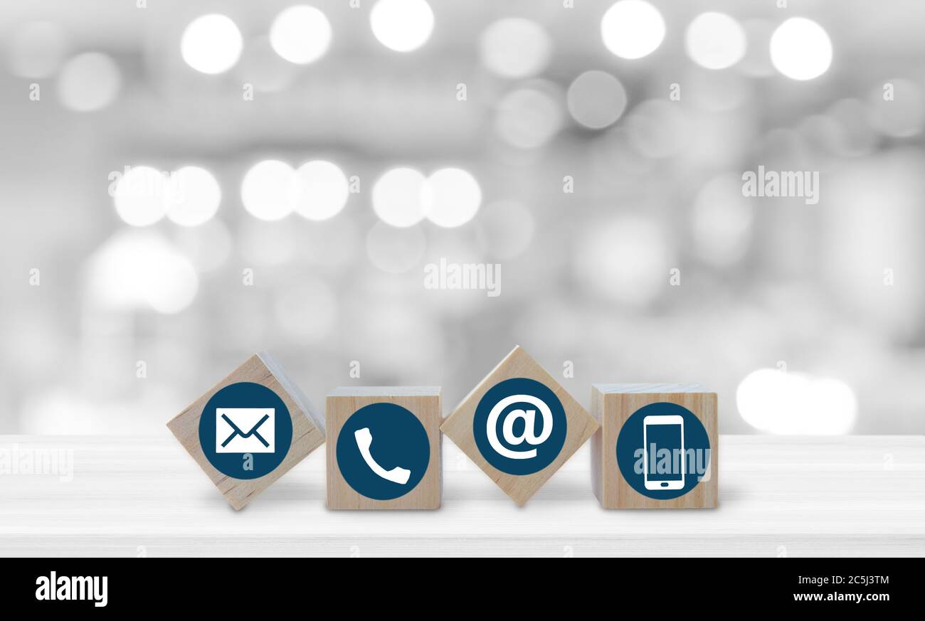 Cube en bois avec icônes de téléphone, d'e-mail et de poste sur une table blanche sur fond flou bokeh clair. Espace de copie. Contactez-nous. Banque D'Images