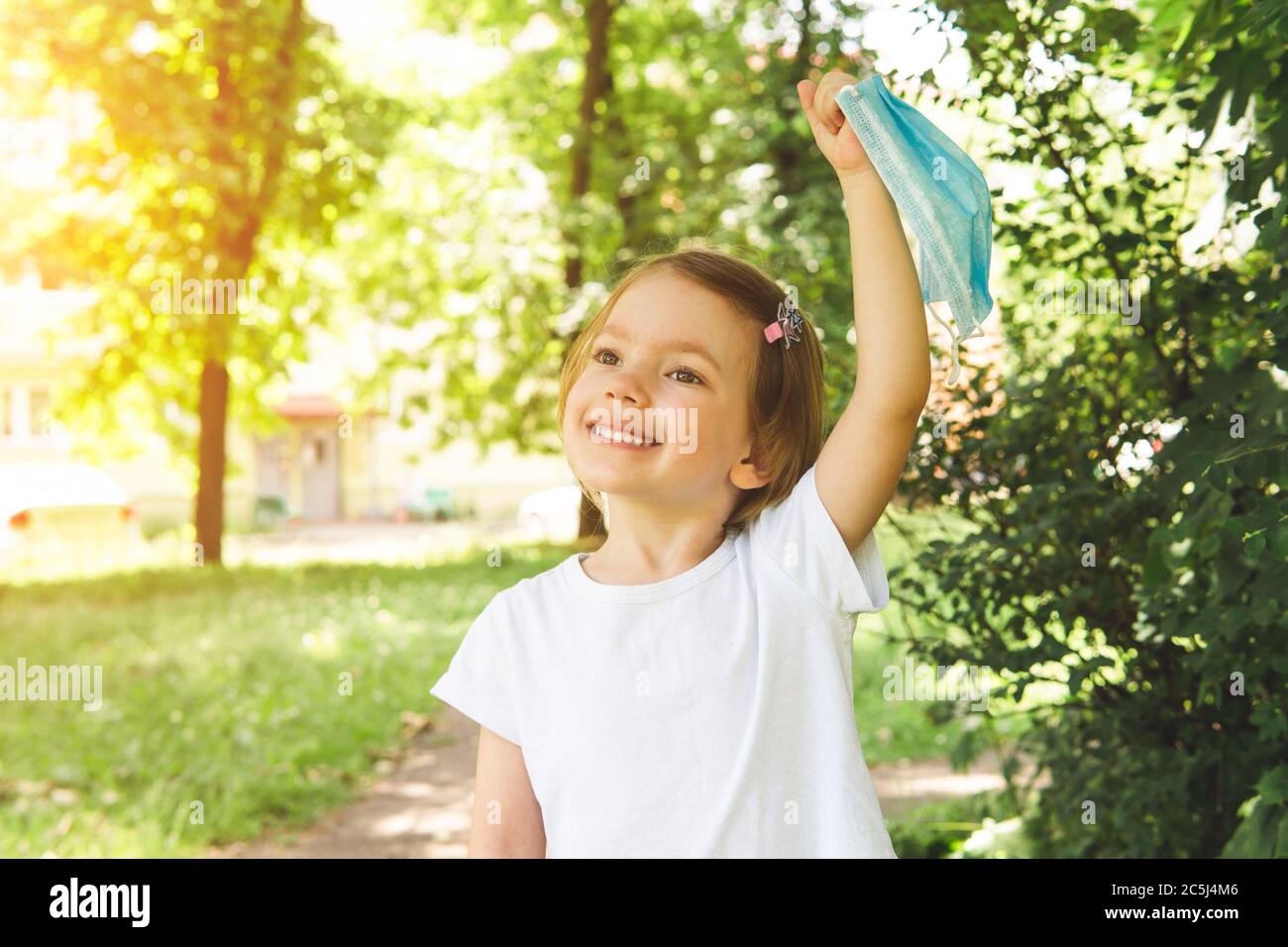 Petite fille mignonne enlever le masque médical avec sourire heureux à l'extérieur, gros plan. Concept de fin heureuse et victoire sur le coronavirus. Banque D'Images