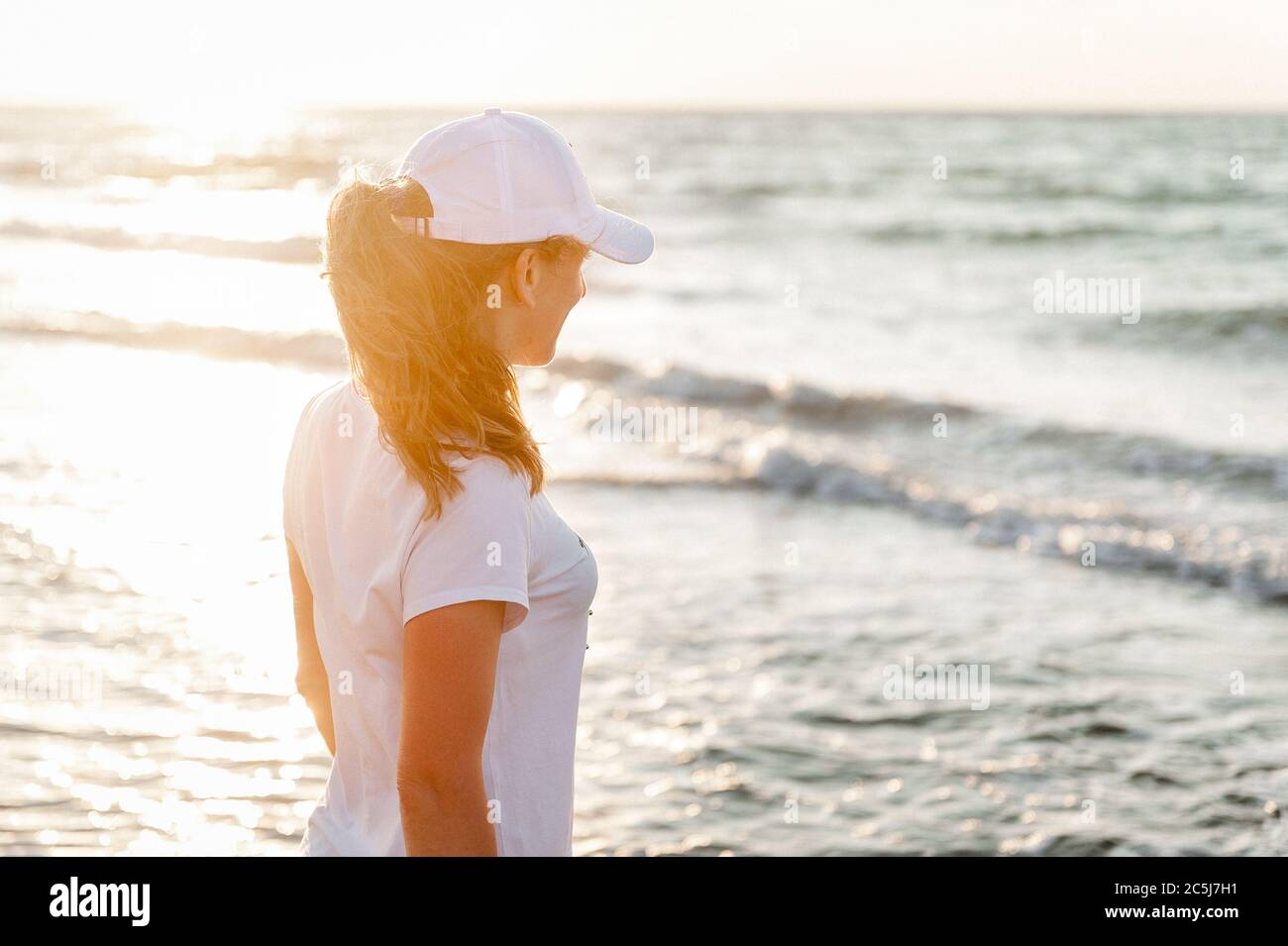 Une jeune athlète contre la mer, dans un T-shirt blanc et une casquette blanche Banque D'Images