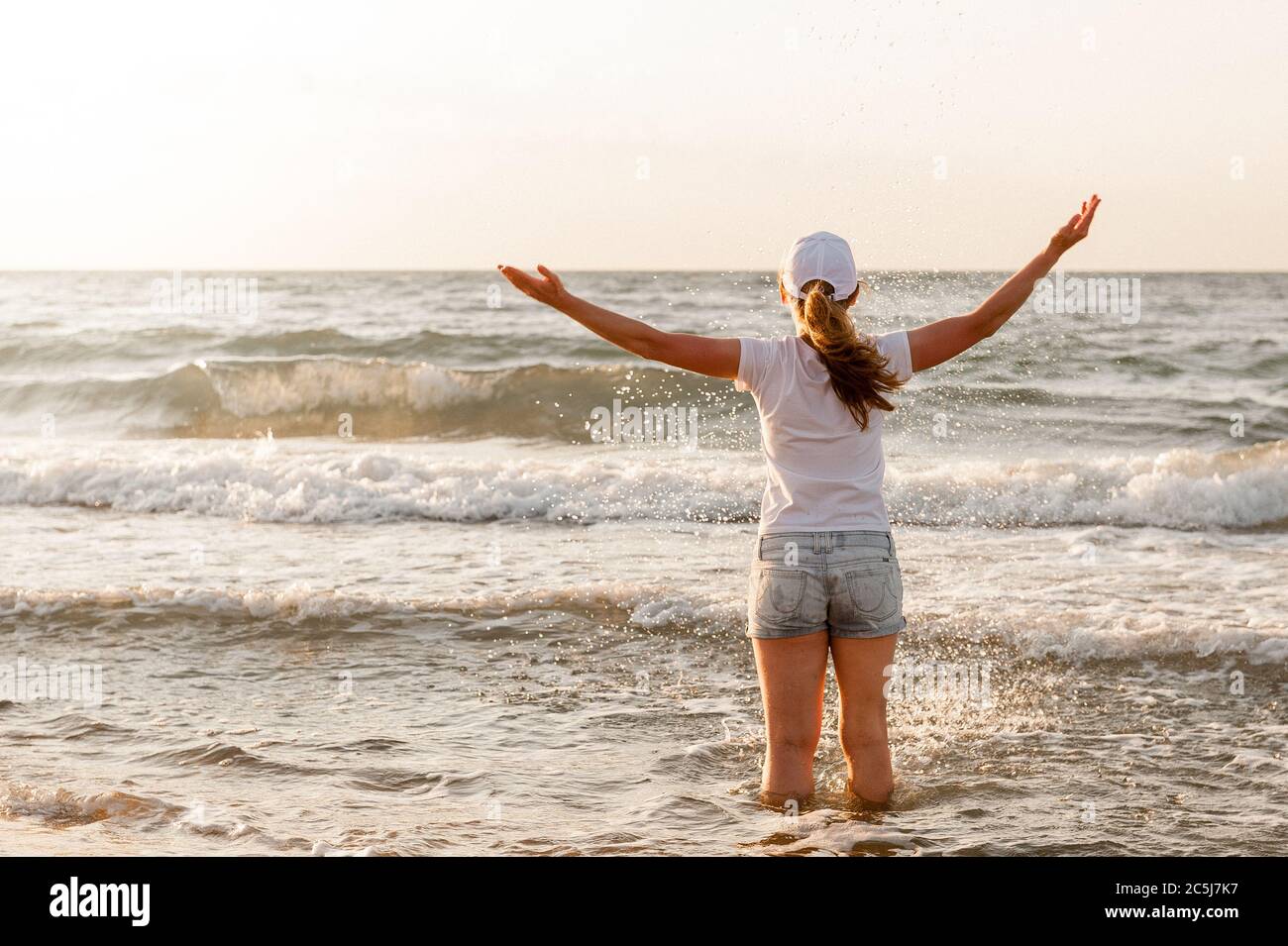 Une fille dans un T-shirt blanc et une casquette se tient contre la mer Banque D'Images