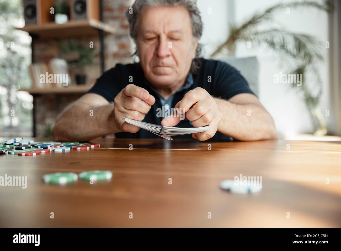 Passionnant. Joyeux homme mature jouant des cartes et buvant du vin avec des amis. Il a l'air ravi, enthousiaste. Homme caucasien jouant à la maison. Émotions sincères, bien-être, expression faciale concept. Bon vieux. Banque D'Images