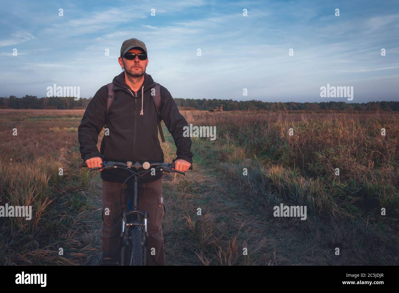 Un homme sur un vélo sur une route de terre, un soir d'automne Banque D'Images