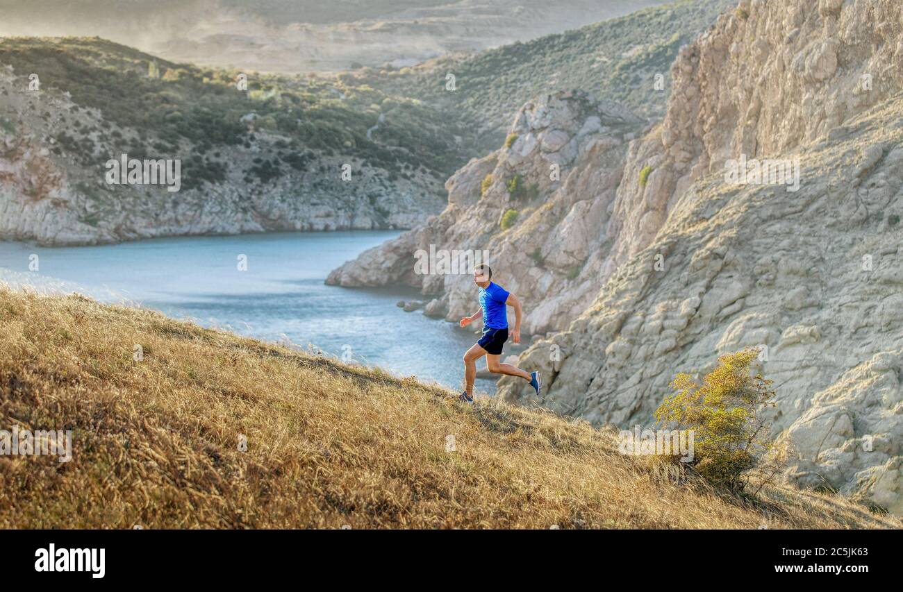 homme athlète courant en amont de la baie de mer et rochers au coucher du soleil Banque D'Images
