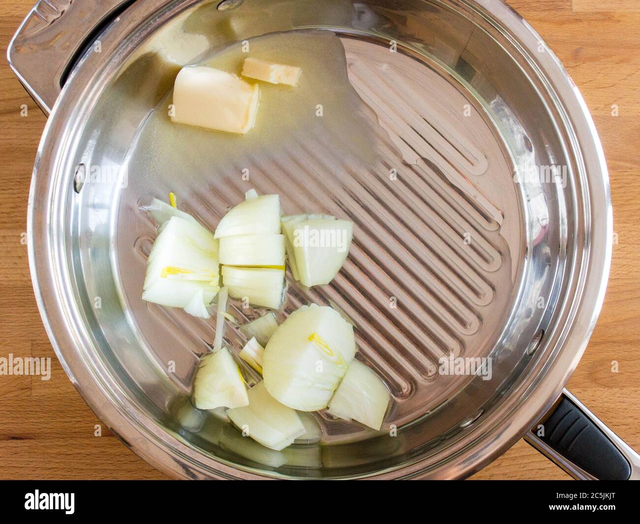 Tranchez les oignons dans une casserole avec du beurre. Ustensiles en métal avec ingrédients, vue du dessus. Banque D'Images