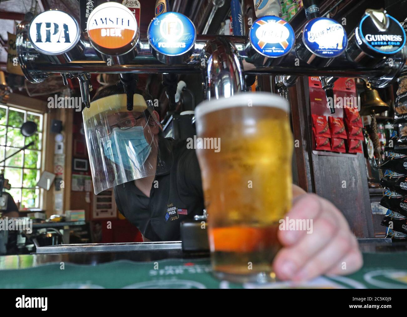 Le Barman Michael Fitzsimons porte un EPI tout en versant une pinte lors des dernières préparations au pub Fullback, dans le nord de Londres, avant sa réouverture, alors que la levée des restrictions de verrouillage supplémentaires en Angleterre entre en vigueur samedi. Banque D'Images