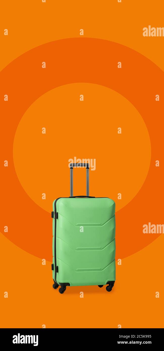 Valise en plastique avec roulettes. Valise à bagages en plastique vert isolée sur fond orange. Impressions de nouveaux lieux. Concept de voyage. Modèle vide Banque D'Images