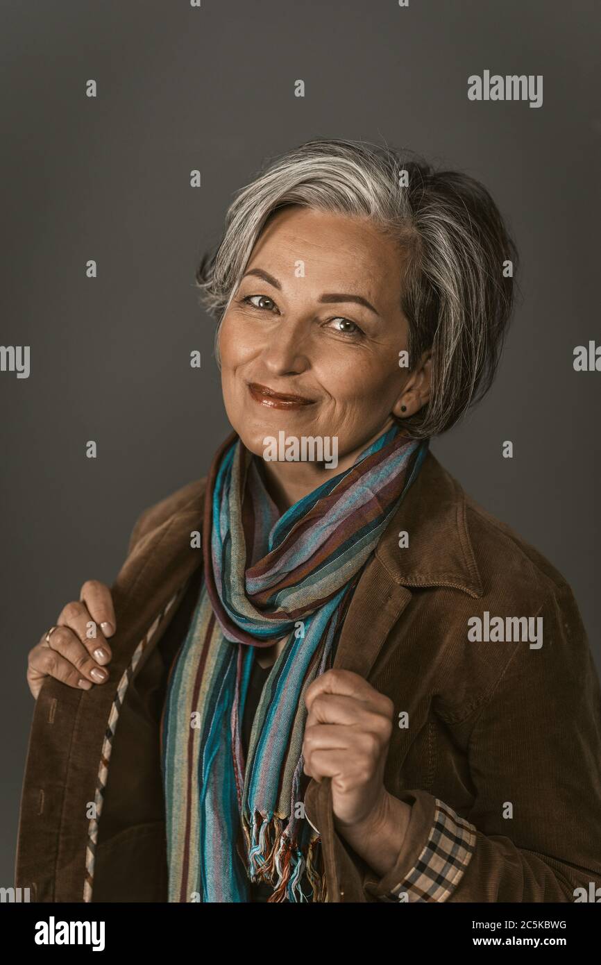 Femme mûre souriante dans une ambiance décontractée. Portrait de femme sur gris. Femme portant un foulard coloré et une veste souriant regardant l'appareil photo. Image teintée Banque D'Images