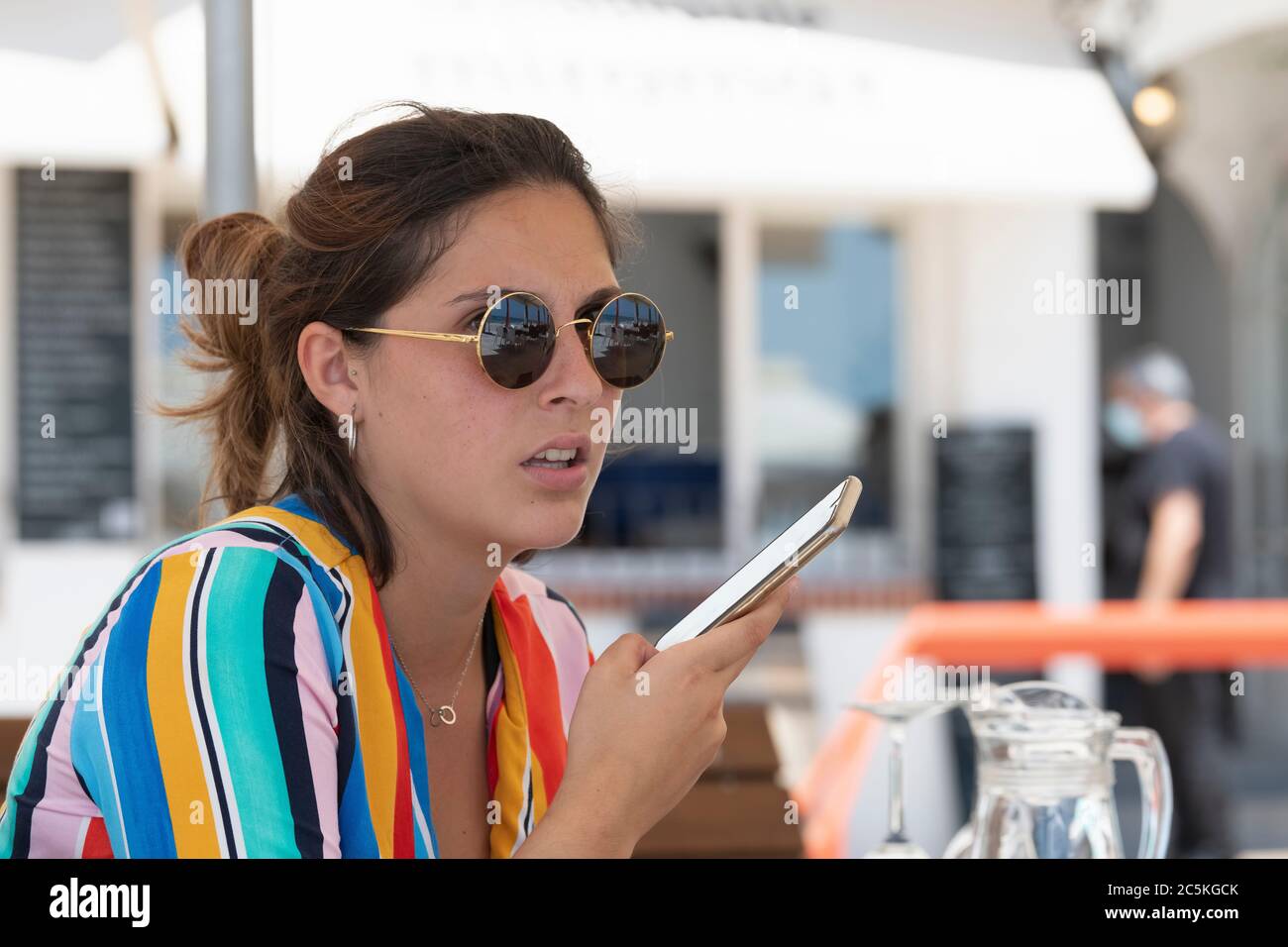 Gros plan d'une jeune femme pensive, belle, portant des lunettes et écoutant son téléphone sur un arrière-plan défocalisé. Vacances et communication c Banque D'Images