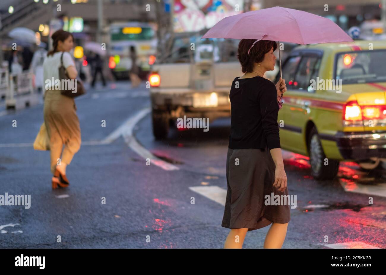 Femme avec parapluie traversant la route dans la rue Shibuya pendant une nuit de pluie, Tokyo, Japon Banque D'Images