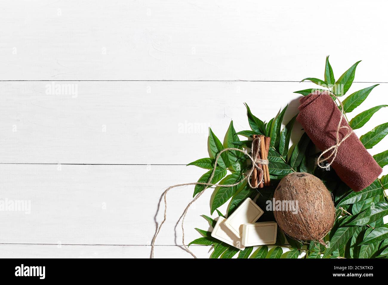 Savons naturels faits à la main avec cannelle, serviette brune, noix de coco et feuilles vertes sur fond de bois blanc Banque D'Images