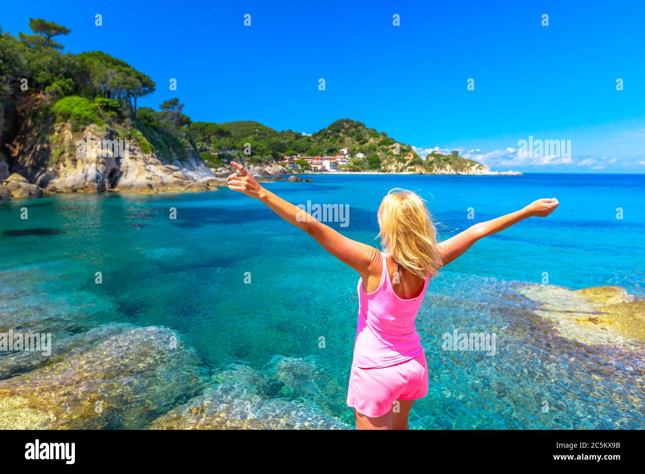 Bonne femme aux bras ouverts en robe rose appréciant à Cotoncello Beach près de la populaire plage Sant 'Andrea, île d'Elbe. Blonde touriste en vacances en Italie Banque D'Images
