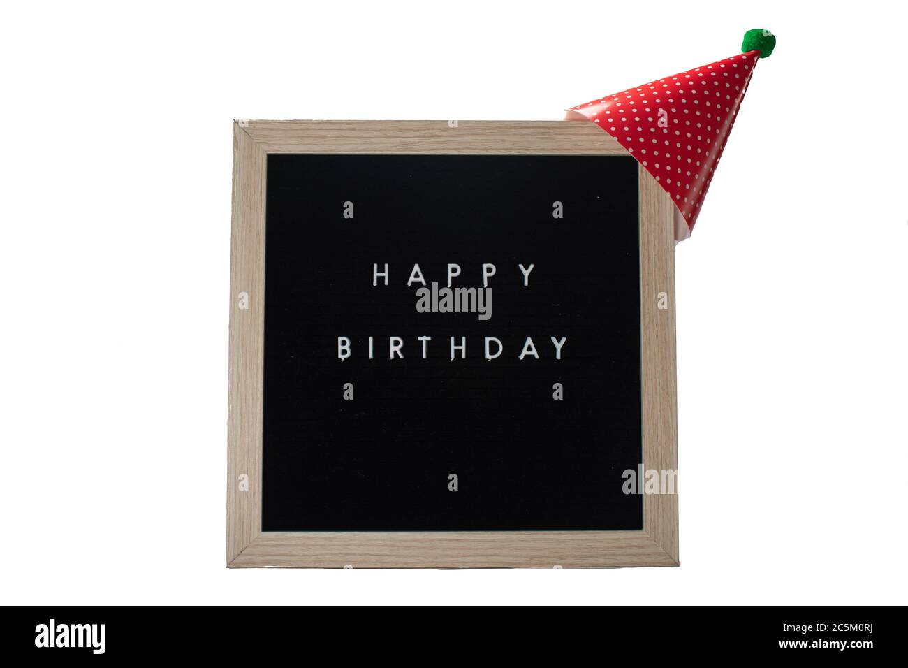 Un panneau noir avec un cadre à motif bouleau qui dit joyeux anniversaire avec un chapeau d'anniversaire rouge et une balle de coton vert sur un fond blanc pur Banque D'Images