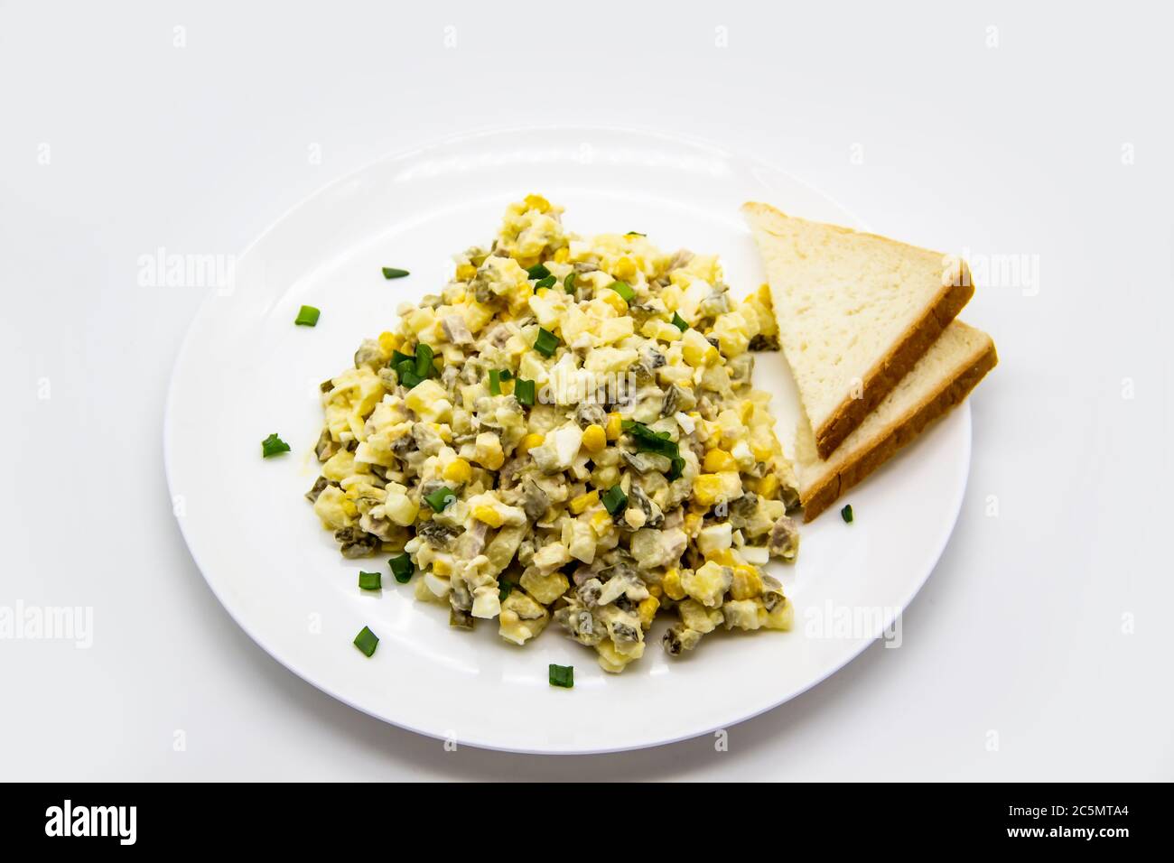 Salade ukrainienne et russe Olivier selon une nouvelle recette sur une assiette blanche. Salade saine Olivier avec viande, maïs et tranches de pain blanc. Délique Banque D'Images