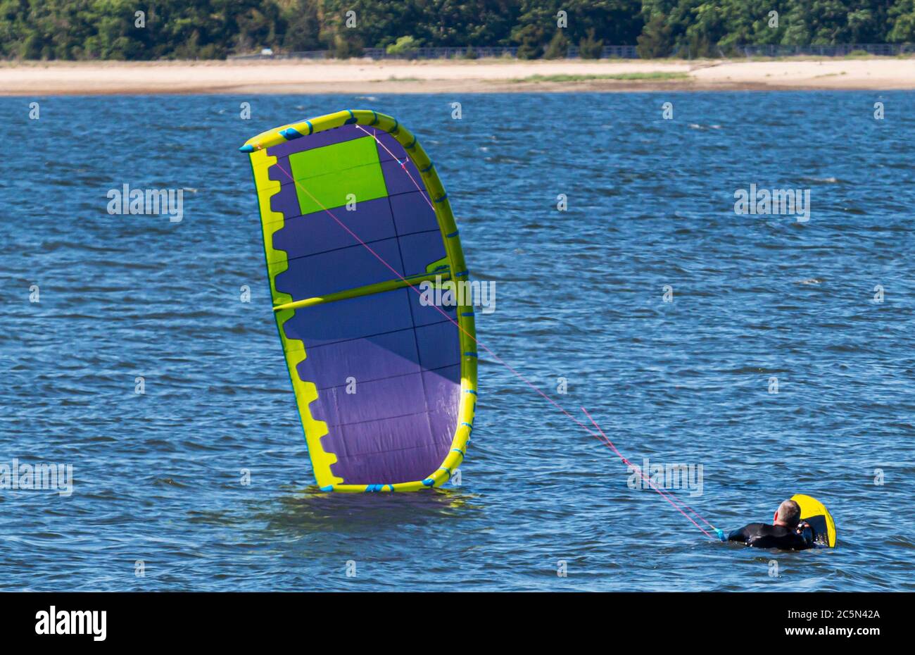 Un homme est sur son conseil prêt pour son cerf-volant pour commencer le kite embarquement dans la baie. Banque D'Images