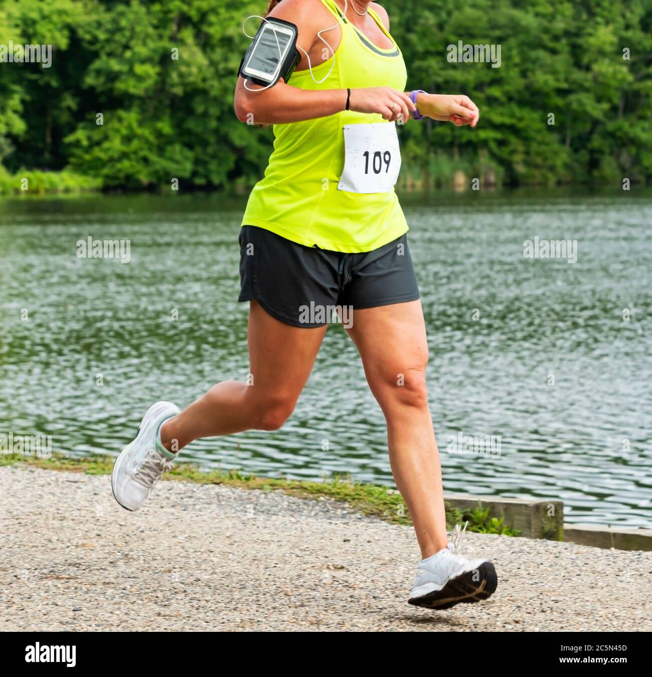 Un coureur courir une course de 10K dans le village de Babylone portant un téléphone cellulaire sur son bras passant l'étang de Southards en été. Banque D'Images