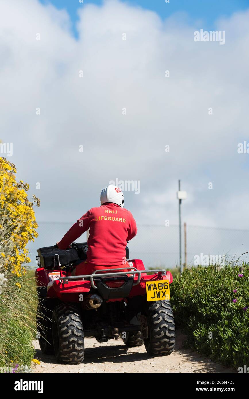 Un garde de la RNLI à bord d'un quad le long du sentier côtier à Fistral à Newquay, en Cornouailles. Banque D'Images