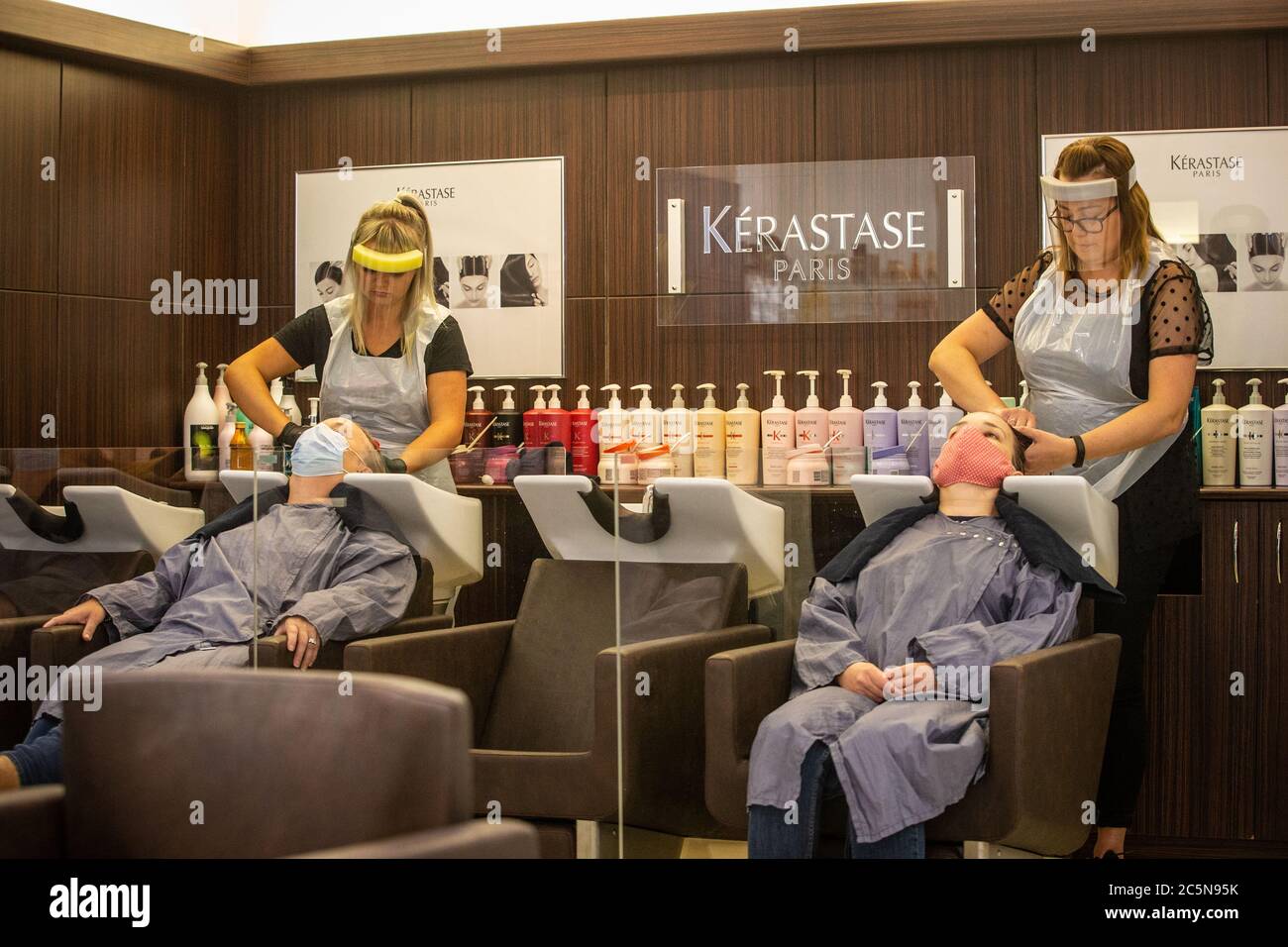 Les coiffeurs en EPI visage visières laver les cheveux de deux clients dans les masques au cours des premiers jours de l'assouplissement de verrouillage en Angleterre pendant la pandémie Covid Banque D'Images